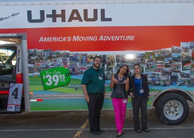 Three people posing in front of a U-Haul truck.