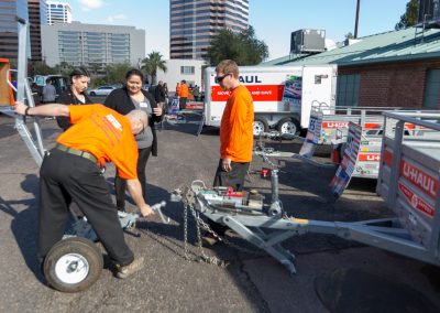 People watching two men connect a U-Haul utility trailer to a trailer dolly.