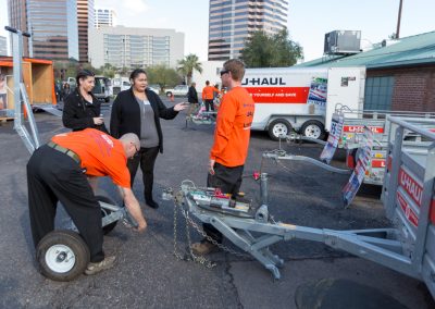 People watching two men connect a U-Haul utility trailer to a trailer dolly.