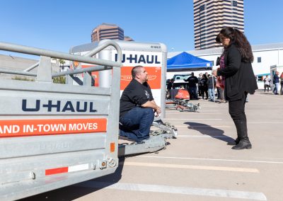 A man sitting on a U-Haul trailer talking to a woman.