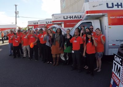 A small group of people posing in front of several U-Haul trucks.